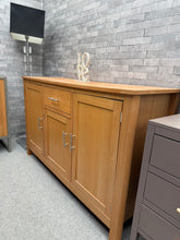 Load image into Gallery viewer, A functional oak effect sideboard offering practical storage with one drawer and three cupboards. Shows signs of use with surface marks and a bowed top, but remains structurally sound. Ideal for those seeking affordable, usable storage furniture with character. The handle needs some TLC.

Delivery Available

Overall Dimensions

140cm wide x 44.5cm deep x 86cm high

