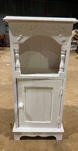 Load image into Gallery viewer, A solid pine bedside table with a white painted finish that shows honest wear from previous use. The design includes a lower cupboard with a single shelf for storage, complemented by an open cubby compartment on the surface above. The existing paintwork could benefit from refreshing, giving you the chance to customise it to suit your bedroom style.

Delivery Available

Overall Dimensions

41cm wide x 24cm deep x 91cm high

