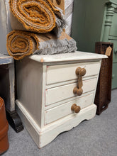 Load image into Gallery viewer, This charming solid pine bedside table features a white finish with distressed detailing that adds character and vintage appeal. Three spacious drawers provide practical storage for essentials within easy reach. Structurally sound and well-maintained, it's ready to enhance any bedroom with both style and functionality.

Delivery Available

Overall Dimensions

48cm wide x 37cm deep x 46cm high

