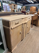 Load image into Gallery viewer, Art Deco sideboard in oak, stripped back to reveal its natural grain and patina. Features two dovetail-jointed drawers and two single cupboards providing generous storage. Structurally sound with original detailing intact. The piece shows honest wear consistent with age—minor surface marks add to its vintage character. The natural finish may benefit from waxing to maintain protection and lustre. A striking statement piece for period interiors or eclectic modern spaces.

Delivery Available

Overall Dimension
