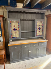 Load image into Gallery viewer, This substantial pine dresser combines practical storage with classic appeal. Structurally sound and in good overall condition, it features two shelves in the upper section alongside two stained glass-fronted cupboards, while the lower section offers four long drawers plus two single and two double cupboards—ideal for displaying and storing tableware, linens, and household items. As a pre-loved piece, it bears the gentle marks of age and use, adding to its character. The dresser disassembles into two sectio
