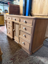 Load image into Gallery viewer, A beautiful stripped mahogany desk revealing the wood's natural grain and character. Features nine dovetail-jointed drawers and a single cupboard, offering generous storage for a workspace. The piece has been stripped to bare wood and would benefit from a protective wax finish. Shows honest patina with minor marks, including missing trim and a side crack—cosmetic imperfections that don't affect functionality. Ideal for those who appreciate authentic vintage furniture with character and craftsmanship.

Deliv
