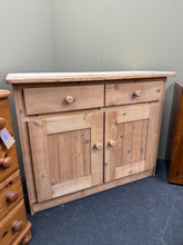 Load image into Gallery viewer, A charming stripped pine sideboard revealing beautiful natural wood grain throughout. Two spacious drawers sit above a generous double cupboard with internal shelf, offering excellent storage for dining rooms or living spaces. The bare wood finish showcases authentic character and patina, ready to be finished with wax or oil to suit your décor and protect the surface. A versatile piece that brings warmth and rustic appeal to any home.

Delivery Available

Overall Dimensions

113cm wide x 48.5cm deep x 90cm 

