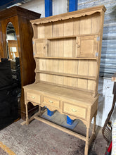 Load image into Gallery viewer, This solid oak dresser has been stripped back to reveal its natural beauty and grain. Structurally sound with excellent storage: four shelves and two cupboards in the upper section, plus three dovetail-jointed drawers below. The bare wood may benefit from a protective wax finish. Splits into two pieces for convenient transport and placement.

Delivery Available

Overall Dimensions

125cm wide x 41cm deep x 189cm high&nbsp;

