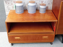 Load image into Gallery viewer, Vintage G Plan teak TV unit in structural condition with only minor cosmetic marks. Features a practical pull-out tray and spacious storage drawer for media and accessories. Smooth-rolling castors make repositioning effortless. A timeless mid-century piece that combines functionality with classic design appeal.

Delivery Available

Overall Dimensions

83cm wide x 46cm deep x 53cm high

