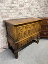 Load image into Gallery viewer, A robust Jacobean oak blanket box built to last. This pre-loved piece combines practical storage with solid craftsmanship—the hinged lid opens to reveal ample space, whilst two dovetail-jointed drawers provide additional organisation at the base. Bearing the expected signs of age and use, it remains in reliable working order with no structural concerns. The removable top section simplifies transport and rearrangement, making it a functional addition to any home seeking authentic, durable furniture with genu
