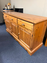 Load image into Gallery viewer, A sturdy solid pine sideboard in excellent structural condition. This classic piece features three dovetail-jointed drawers above a single and double cupboard, providing generous storage for any room. Minor surface marks add character without compromising its solid construction. Ideal for dining rooms, hallways, or living spaces seeking timeless functionality and natural wood appeal.

Delivery Available

Overall Dimensions

152cm wide x 49cm deep x 80cm high

