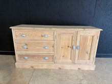 Load image into Gallery viewer, Rustic charm meets practical storage in this low pine sideboard. Stripped back to reveal natural wood grain, it showcases authentic craftsmanship with three dovetail-jointed drawers and a spacious double cupboard. The bare finish invites personalisation—a coat of wax or oil will enhance the wood's character and provide lasting protection. Perfect for hallways, dining rooms, or living spaces seeking vintage appeal with genuine functionality.

Delivery Available

Overall Dimensions

123cm wide x 41cm deep x 6
