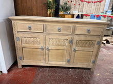 Load image into Gallery viewer, A characterful stripped oak sideboard with solid bones and honest patina. Three dovetail-jointed drawers sit above a double and single cupboard, offering practical storage. The piece is structurally sound and fully functional, though it bears the marks of age—a split is present on the top and some veneer shows wear. A protective wax finish would enhance the stripped oak and help preserve it for years to come.&nbsp;

Delivery Available

Overall Dimensions

136.5cm wide x 43.5cm deep x 86.5cm high

