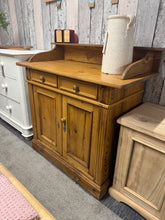 Load image into Gallery viewer, A charming vintage pine washstand that doubles as a sideboard, offering both character and practicality. Built to last, this piece shows its age with minor surface marks that add to its authentic appeal. The layout features two decorative faux drawers positioned above a spacious double cupboard, providing ample storage. Structurally solid and ready for everyday use, it's an ideal addition for those seeking genuine vintage furniture with genuine patina.

Delivery Available

Overall Dimensions

99cm wide x 50
