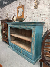 Load image into Gallery viewer, A striking hardwood bookcase featuring a beautiful blue distressed finish that adds character to any room. The piece combines display space with practical storage—one fixed shelf for showcasing books and décor, plus three small drawers for keeping items organised and out of sight. Structurally sound and in good condition, this statement piece brings vintage charm and functionality to your home.

Delivery Available

Overall Dimensions

130cm wide x 40cm deep x 101cm high

