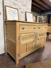 Load image into Gallery viewer, This beautiful stripped oak sideboard showcases the wood's natural grain and character. Returned to bare wood, it may benefit from a protective wax finish to enhance durability. In excellent condition with minimal wear, it offers generous storage through two dovetail-jointed drawers and a lower double cupboard featuring an internal shelf—ideal for displaying or concealing items as needed.

Delivery Available

Overall Dimensions

127cm wide x 49cm deep x 86cm high

