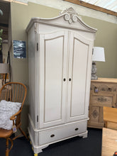 Load image into Gallery viewer, This elegant white ornate style wardrobe combines classic styling with practical functionality. Structurally sound and well-maintained, it features a hanging rail for garments, a spacious drawer for additional storage, and an internal mirror for convenience. The piece disassembles into three sections—drawer, cupboard, and cornice—making transport and placement effortless. Minor marks reflect its character and history. Perfect for adding vintage charm to any bedroom whilst offering genuine storage capacity.

