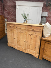 Load image into Gallery viewer, A timeless solid pine sideboard, stripped to reveal its natural grain and character. This piece showcases authentic vintage charm with its honest patina and minor marks—testament to its genuine heritage.
Featuring three dovetail-jointed drawers above a single and double cupboard, it offers generous storage for dining rooms, hallways, or living spaces. The natural finish invites personalisation; a coat of wax or oil will enhance protection and deepen the wood's warmth, or leave it as-is for rustic appeal.
St
