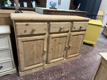 Load image into Gallery viewer, This stripped pine sideboard showcases the wood's natural character and grain. Featuring three short drawers positioned above a double cupboard and single cupboard, it offers versatile storage for dining rooms or living spaces. The piece is structurally sound and in good condition. To enhance protection and bring out the wood's warmth, consider applying a quality wax finish.&nbsp;

Delivery Available

Overall Dimensions

134cm wide x 41cm deep x 92cm high

