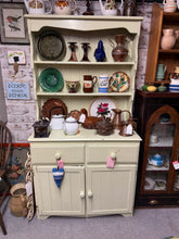 Load image into Gallery viewer, Charming pine dresser featuring a soft sage green finish with distressed patina throughout. The spacious design includes open shelving at the top, two practical drawers, and a double cupboard base—ideal for bedroom or dining room storage. Please note: one cupboard door requires adjustment and doesn't fully close. The piece disassembles into two sections for convenient transport and repositioning. Perfect for those who appreciate character-filled, lived-in furniture or as a project piece for refinishing enth
