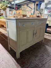 Load image into Gallery viewer, A beautifully restored Ercol sideboard, hand-painted in soft sage green using Annie Sloan paint. The top has been sanded and waxed to reveal warm wood tones beneath. Two generous drawers sit above a spacious double cupboard, offering ample hidden storage for dining essentials or living room display. Structurally sound with excellent bones, this classic mid-century piece strikes the perfect balance between statement-making charm and understated elegance. A versatile addition to contemporary or traditional in
