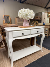 Load image into Gallery viewer, A classic French-style console table in crisp white, perfect for making a sophisticated statement in your entryway or hallway. Features two practical drawers and a lower shelf for storing keys, mail, and decorative pieces. Structurally sound with the authentic patina of a well-loved piece—minor marks only add to its vintage charm. An elegant focal point for smaller spaces that combines storage with understated elegance.

Delivery Available

Overall Dimensions

100cm wide x 33cm deep x 79cm high

