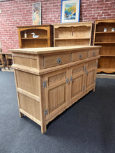 Load image into Gallery viewer, A beautiful stripped oak sideboard, restored to reveal its natural grain and character. The piece features three dovetail-jointed drawers positioned above one single and one double cupboard, providing generous storage for dining rooms or living spaces. Structurally sound and in excellent condition, the bare wood finish offers an authentic vintage aesthetic. A protective coat of wax is recommended to enhance durability and bring out the oak's warm tones.

Delivery Available

Overall Dimensions

136cm wide x 
