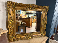 Load image into Gallery viewer, This beautiful large gilt-framed mirror adds a touch of timeless elegance to any room. Featuring a bevelled edge that enhances its classic appeal, the mirror is structurally solid and well-maintained. While it is a pre-loved piece with a few minor marks, these subtle signs of character only add to its charm. Perfect for brightening spaces and creating a sense of openness, this mirror combines vintage style with practical function, making it a delightful addition to your home décor.

Delivery Available

Over
