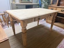Load image into Gallery viewer, A characterful solid pine dining table with authentic stripped finish, revealing the wood's natural grain and patina. The rustic surface bears gentle marks that add to its charm and heritage appeal. Practical and spacious, this table comfortably seats six and features a front drawer for convenient storage. The removable legs make it easy to transport and reposition. While the stripped pine finish is beautiful as-is, a protective coat of wax will enhance durability and deepen the wood's warmth. Ideal for tho

