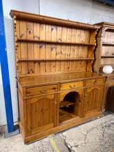 Load image into Gallery viewer, This beautiful solid pine dresser is sturdy and well-maintained. While it shows some minor marks, they aren&#39;t major. It offers plenty of storage space with three dovetail-jointed drawers above two cupboards and a shelf. The upper section includes two additional shelves. For convenience, the top separates from the base, making it easier to move.

Overall Dimensions

173cm wide x 57cm deep x 188cm high

DELIVERY AVAILABLE      

HAVE THIS PAINTED A COLOUR OF YOUR CHOICE FOR AN EXTRA £120 OR HAVE IT COMPLETELY

