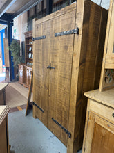 Load image into Gallery viewer, A striking rustic double wardrobe built to last. Structurally sound with solid construction throughout, this piece features one internal hanging rail for convenient clothing storage. It has a few marks to the metalwork but nothing major. Please note: this is a heavy item that does not disassemble for moving.

Delivery Available

Overall Dimensions

114cm wide x 61cm deep x 187cm high

