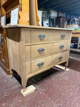 Load image into Gallery viewer, A beautiful Art Nouveau oak chest of drawers, stripped back to reveal its natural grain and character. Three spacious dovetail-jointed drawers provide generous storage. Structurally sound and in excellent condition. The bare wood finish showcases authentic craftsmanship and allows you to personalise with your choice of wax or oil for protection.

Delivery Available

Overall Dimensions

107cm wide x 49.5cm deep x 79cm high&nbsp;

