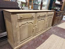 Load image into Gallery viewer, Crafted from oak, this sideboard showcases authentic character with its stripped-back finish. While the wood displays minor surface marks and some drawer discolouration—which can be typical of reclaimed pieces—these can be easily concealed with a protective wax treatment. The piece features three dovetail-jointed drawers positioned above a double cupboard and single cupboard, offering practical storage with traditional joinery craftsmanship. A light finishing coat will restore its lustre and protect the nat
