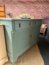 Load image into Gallery viewer, A striking solid wood sideboard finished in 'Steaming Green' by Frenchic. This well-constructed piece combines style with practical storage—featuring two dovetail-jointed drawers above a double cupboard with internal shelving. Ideal for living rooms or dining spaces seeking a bold statement accent. In good overall condition with minor surface marks that add character.

Delivery Available

Overall Dimensions

127.5cm wide x 55.5cm deep x 96cm high

