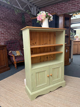 Load image into Gallery viewer, A charming solid pine bookcase with a subtle green distressed finish that adds character to any room. Two open shelves provide display space for books and décor, while the double cupboard below offers concealed storage. Structurally sound and in good condition, this piece combines practical storage with vintage-inspired style.

Delivery Available

Overall Dimensions

82cm wide x 31cm deep x 122cm high


