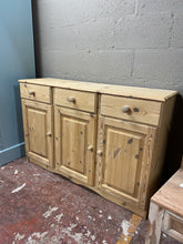 Load image into Gallery viewer, This delightful solid pine sideboard has been completely stripped back to its natural state. It has 3 short dovetail jointed drawers over a large cupboard with 1 long shelf in. It is used and does have a few minor marks but nothing too major. It may need a coat of wax for protection as the wood is bare.

Overall Dimensions

137cm wide x 40cm deep x 89cm high 

DELIVERY AVAILABLE    

For our other items see our website https://fossewayfurniture.co.uk

collection from cv36 or bs36

