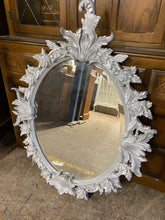 Load image into Gallery viewer, Add a touch of elegance to your home with this beautifully designed silver wall mirror. The beveled edges add a modern touch while the intricate details of leaves and flowers add a timeless charm. This oval mirror is in excellent condition and sturdy enough to last for years to come.  Overall Dimensions  80cm x 107cm      DELIVERY AVAILABLE      For our other items see our website https://fossewayfurniture.co.uk
