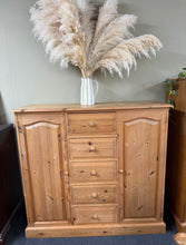 Load image into Gallery viewer, A characterful solid pine cupboard with genuine vintage appeal. Structurally sound and in good working order, this piece shows honest signs of age and use—minor marks that add to its authentic charm rather than detract from it. Features five dovetail-jointed drawers and two cupboards, each fitted with shelves. The craftsmanship is evident in the joinery, while the makeshift shelving added by previous owners speaks to its practical, well-loved history. Ideal for anyone seeking a sturdy, functional storage so
